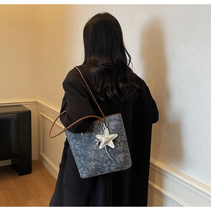 Detail view of printed grey tote bag with brown straps and star charm on model