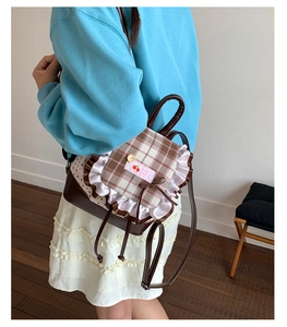Detail eines braunen Karo-Rucksacks mit Kirsch-Patches und Spitzenbesatz auf der Schulter