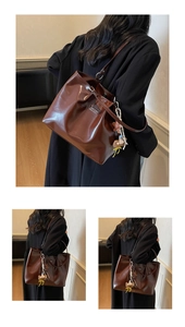 Detail of coffee brown glossy tote bag with metal logo and plush bear accessory charm