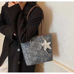 Detailed macro view of gray printed tote bag featuring metallic star pendant and brown strap