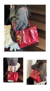 Detail view of a large red glossy tote bag with a teddy bear charm for daily commuting