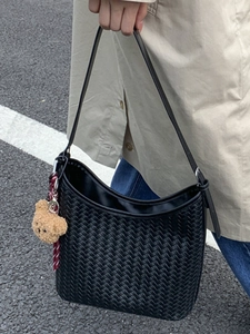 Sac seau noir tissé à la main avec un charm d'ours brun sur fond de rue urbaine