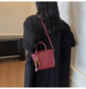 Details der burgunderroten Bucket Bag mit Ethno-Perlenanhänger und goldener Hardware