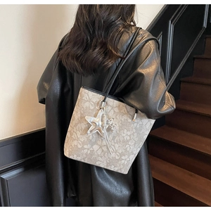 Close-up of beige tote bag with clover patterns and star pendant on a leather coat