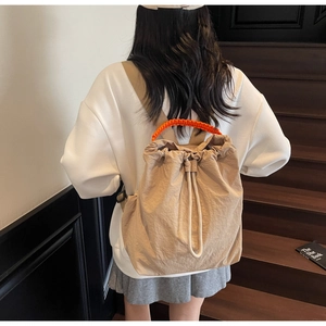 Detail of drawstring backpack showing orange woven handle and adjustable straps on stairs