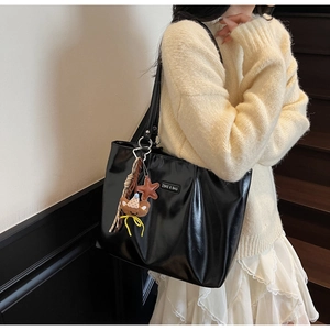 Detail of black glossy tote bag with brand logo and cute star bear pendant charms