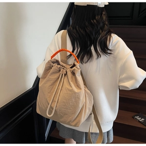 Detail of beige drawstring backpack with contrasting orange rope handle and nylon texture