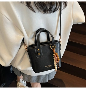 Detail der schwarzen Mini-Leder-Beuteltasche mit Retro-Perlenanhänger auf Holzgrund