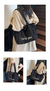 Detail view of black corduroy tote bag showing side pockets and white embroidered text