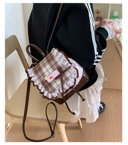 Detail eines süßen braun karierten Mini-Rucksacks mit weißem Spitzenrand und Kirsch-Label