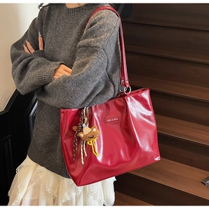 Detailed shot of large red glossy leather tote bag with a brown knit bear charm