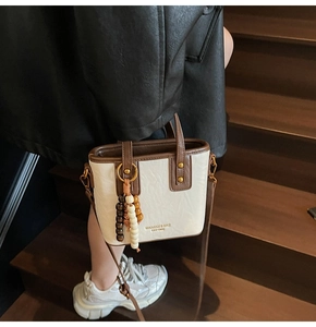 Detailaufnahme der weißen Beuteltasche mit Holzperlen-Anhänger und goldener Aufschrift