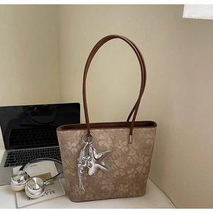 Brown floral tote bag with silver star charm next to a laptop and headphones