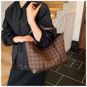 Side view of a large brown checkerboard tote bag with leather straps worn by a model