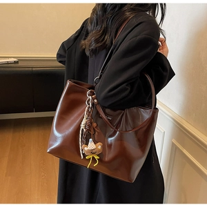 Detail of a brown leather tote bag with a cute bear charm in a classic commute style