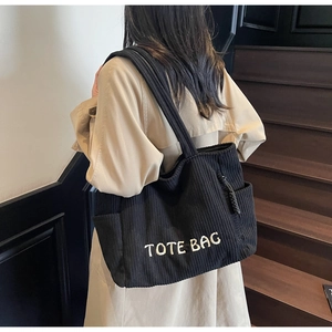 Detail view of black corduroy tote bag featuring white TOTE BAG embroidery and shoulder strap