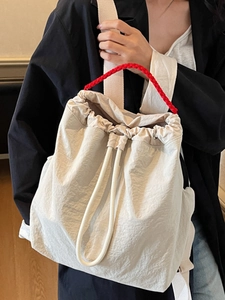 Minimalist beige drawstring backpack with red woven handles and lightweight nylon texture