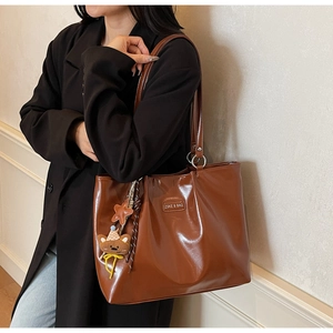 Detail of tan leather tote bag with metal logo and cute bear charm worn by a model