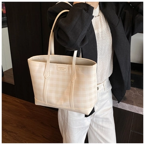 Detail of cream checkerboard tote bag featuring a brown leather logo patch and thin strap