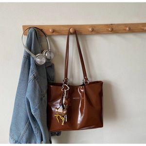 Detail of a brown leather tote bag featuring a plush bear charm and star keychain accessory