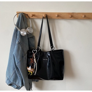 Detail of black PU leather tote bag with brand plaque and heart-shaped plush charm