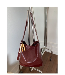 Détail du sac seau bordeaux tressé avec pendentif en perles de bois sur un cintre