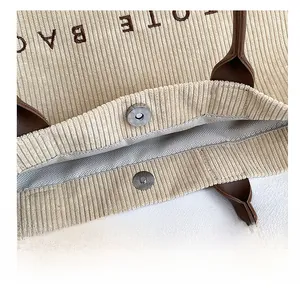 Close-up of the metal magnetic buckle closure on a khaki corduroy tote bag with lining