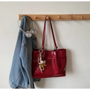 Detail view of deep red glossy leather tote bag with charm on a wooden coat rack