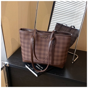 Close-up of brown checkerboard tote bag with square brand plaque on a black surface