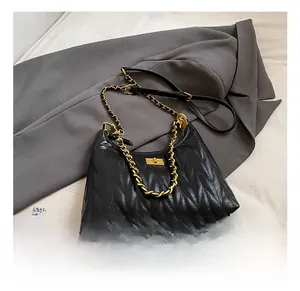 Detail of black quilted shoulder bag featuring V-shaped texture and gold chain strap