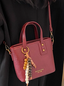 Dunkelrote Leder-Eimertasche mit goldenen Nieten und buntem Perlenanhänger-Detail