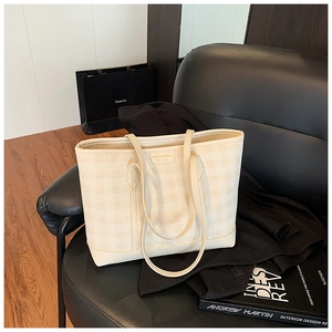 Detail of cream checkerboard tote bag with shoulder straps on a stylish black chair