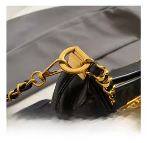 Detailed close-up of golden metal D-ring and chain strap on black quilted leather handbag