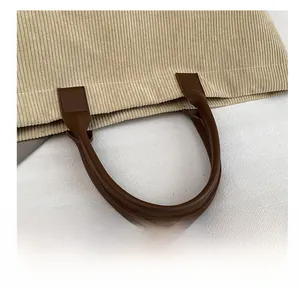 Detail of beige corduroy tote with dark brown leather handles and reinforced stitching