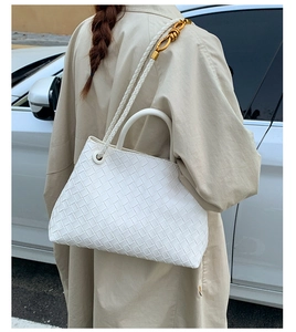 Detail of white woven tote bag with adjustable shoulder strap and gold knot hardware