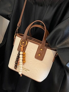 Schicke cremefarbene Beuteltasche mit braunem Besatz, Perlenanhänger und Trageriemen