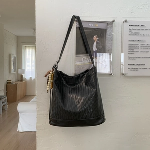 Détail du sac seau tressé noir montrant le tissage en cuir et le pendentif en perles