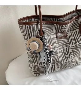 Detail of fabric tote bag with leather trim and decorative straw hat bag charm