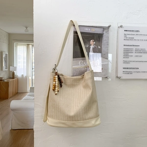 Détail d'un sac seau tressé beige avec breloque en perles et base en cuir durable