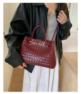 Close-up of burgundy woven leather handbag with gold knot detail and thin shoulder strap