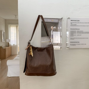 Détail d'un sac hobo tressé marron foncé avec franges en bois sur un mur blanc texturé