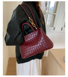 Detailed shot of burgundy woven leather handbag with golden knot buckle on the shoulder strap