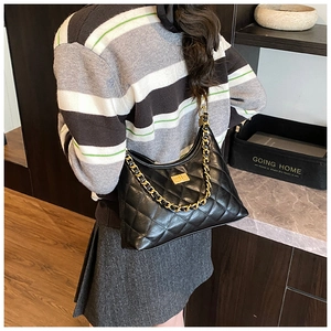 Detail view of black quilted shoulder bag with gold chain strap worn by a model