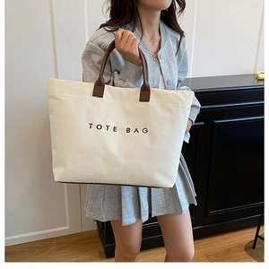 Close-up of white corduroy tote bag featuring brown straps and embroidered TOTE BAG text