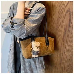 Close-up of brown suede tote bag with a cute teddy bear charm and black handles
