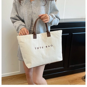 Detail of cream corduroy tote bag with brown leather handles and logo embroidery