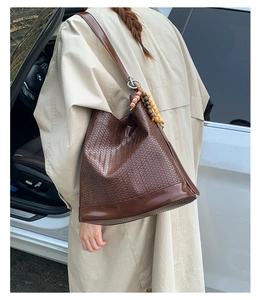 Détail du sac seau tressé marron foncé avec pompons en perles de bois élégants