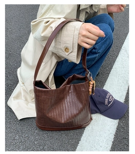 Détail d'un sac seau tressé marron foncé avec bandoulière et pendentif en perles ethniques