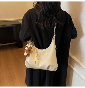 Détail du sac sous le bras blanc crème avec un joli charme d'ours en peluche brun