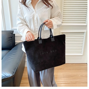 Close-up of black corduroy tote bag with textured TOTE BAG lettering and sturdy handles